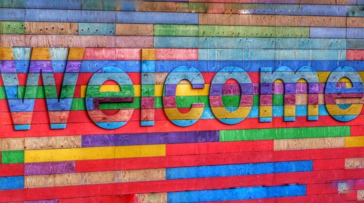 The word Welcome is writte from multicolored wooden boards, against a similarly colorful board background.